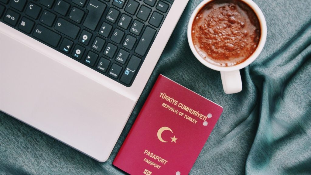 Turkish passport next to a laptop and a cup of Turkish coffee